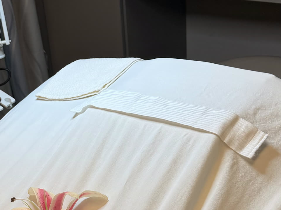 A treatment bed in the esthetics salon, made up with fresh white linens and folded towels.